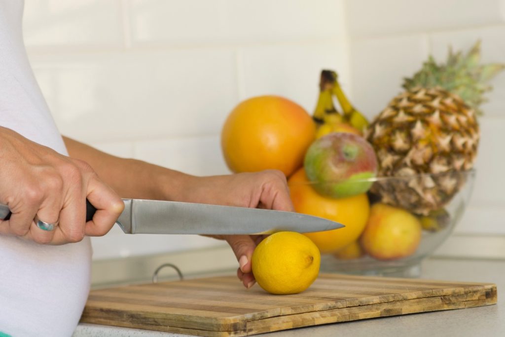 Photo pf pregnant woman slicing a lemon on a cutting board with a chef's knife. 
